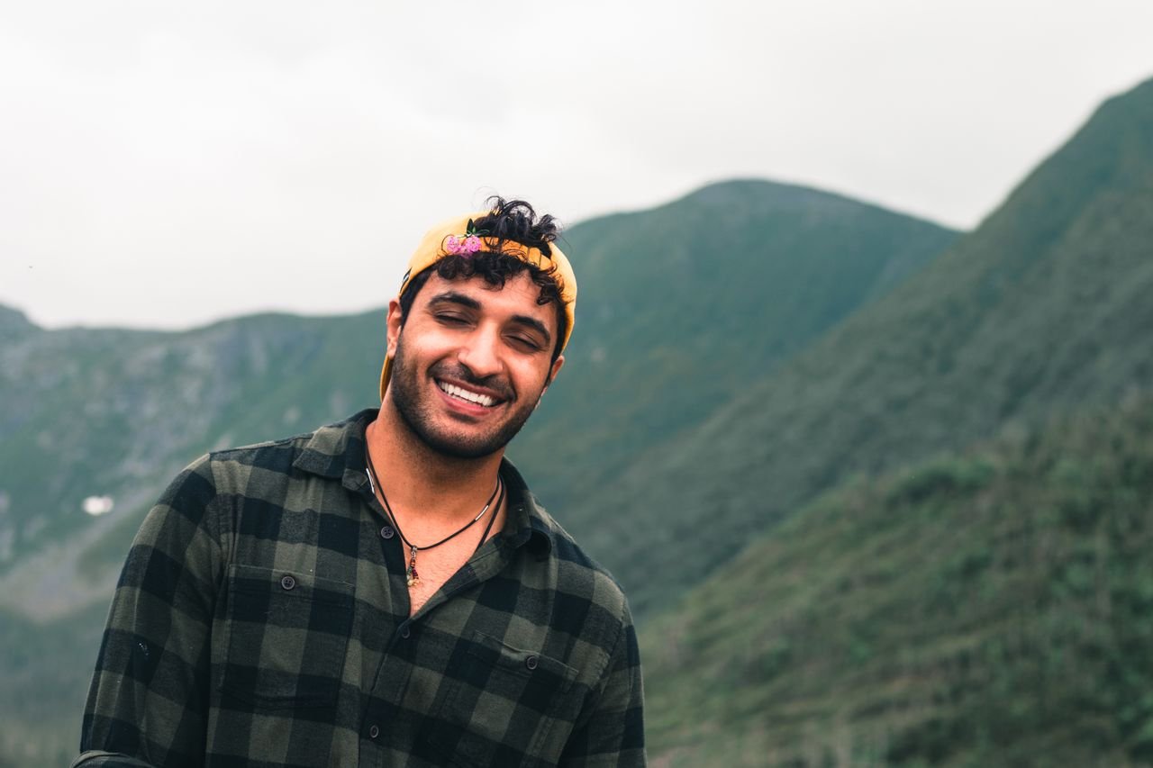 summer-sale Happy man wearing cap and plaid shirt, smiling in front of Quebec's scenic mountains.