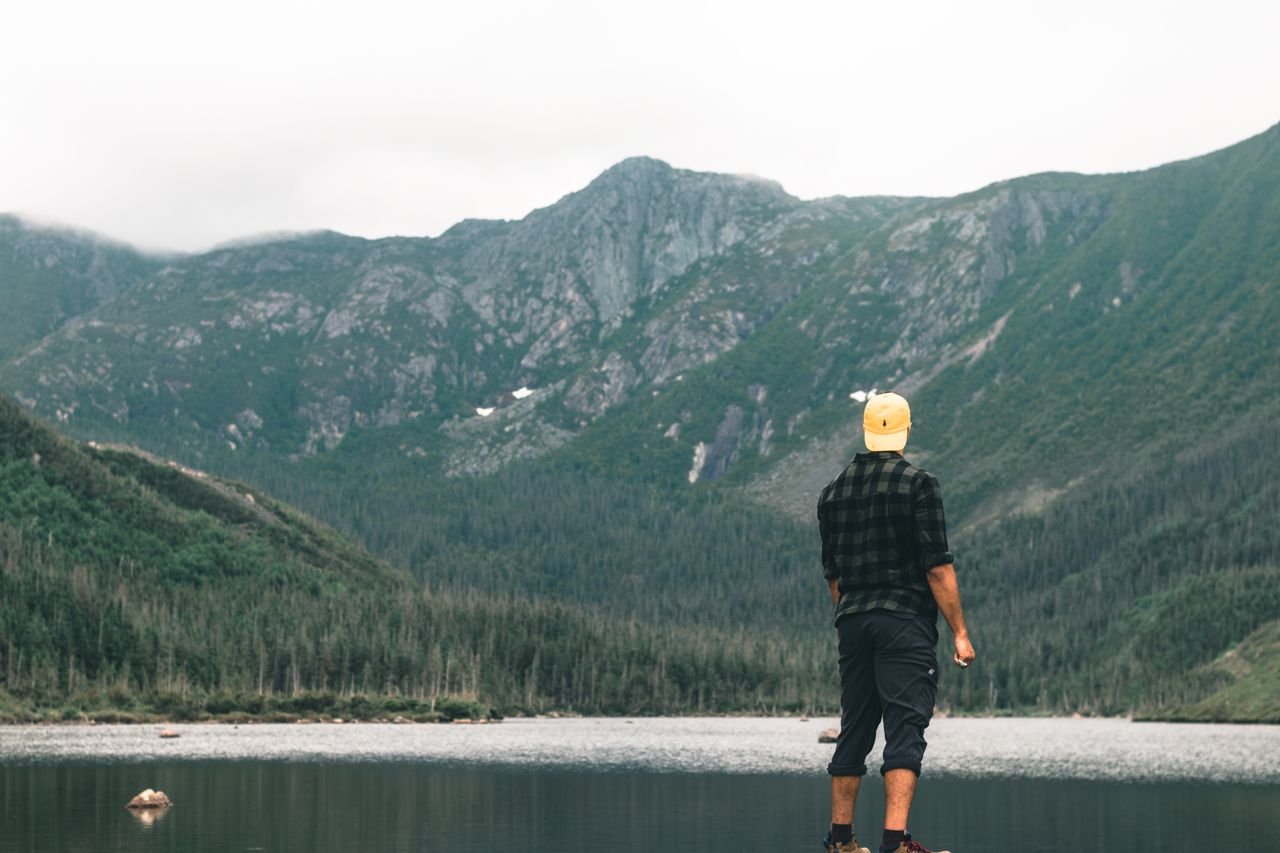 hero-img Man in plaid shirt overlooking scenic mountain view at Sainte-Anne-des-Monts, Canada.