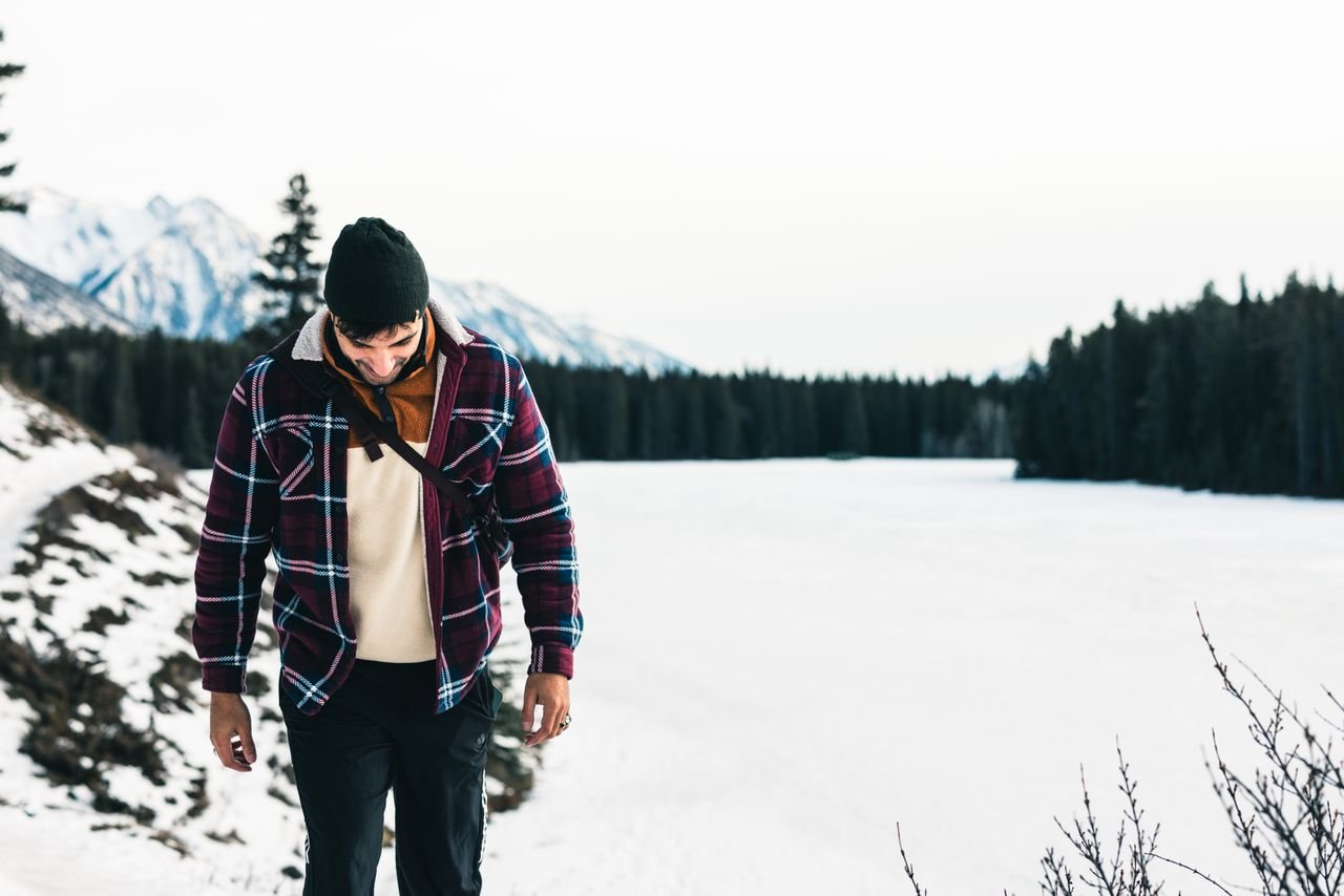 Man hiking by frozen lake in Banff, Canada during winter with scenic mountain view.